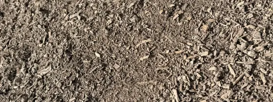 Fine grey-brown screened compost spread flat in sunlight with small bits of wood fiber