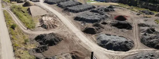 Aerial view of the Casco Organics yard with rows of dark mulch piles, a screener and trucks, and a pond beyond