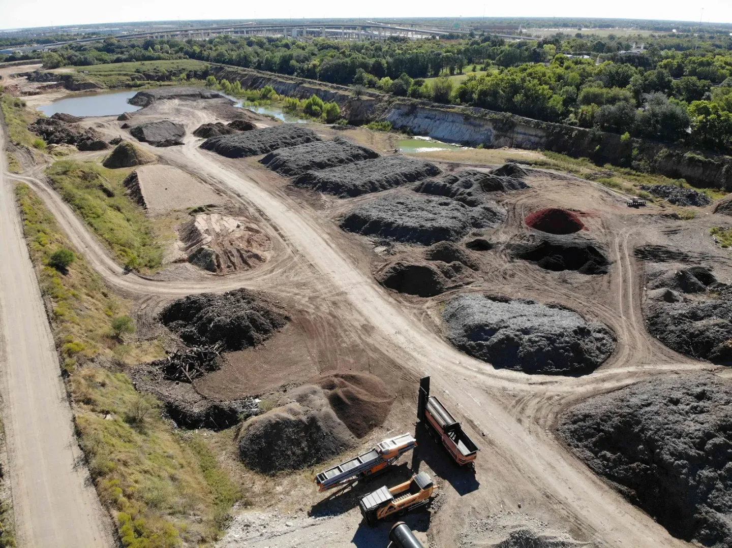Aerial view of the Casco Organics yard with rows of dark mulch piles, a screener and trucks, and a pond beyond